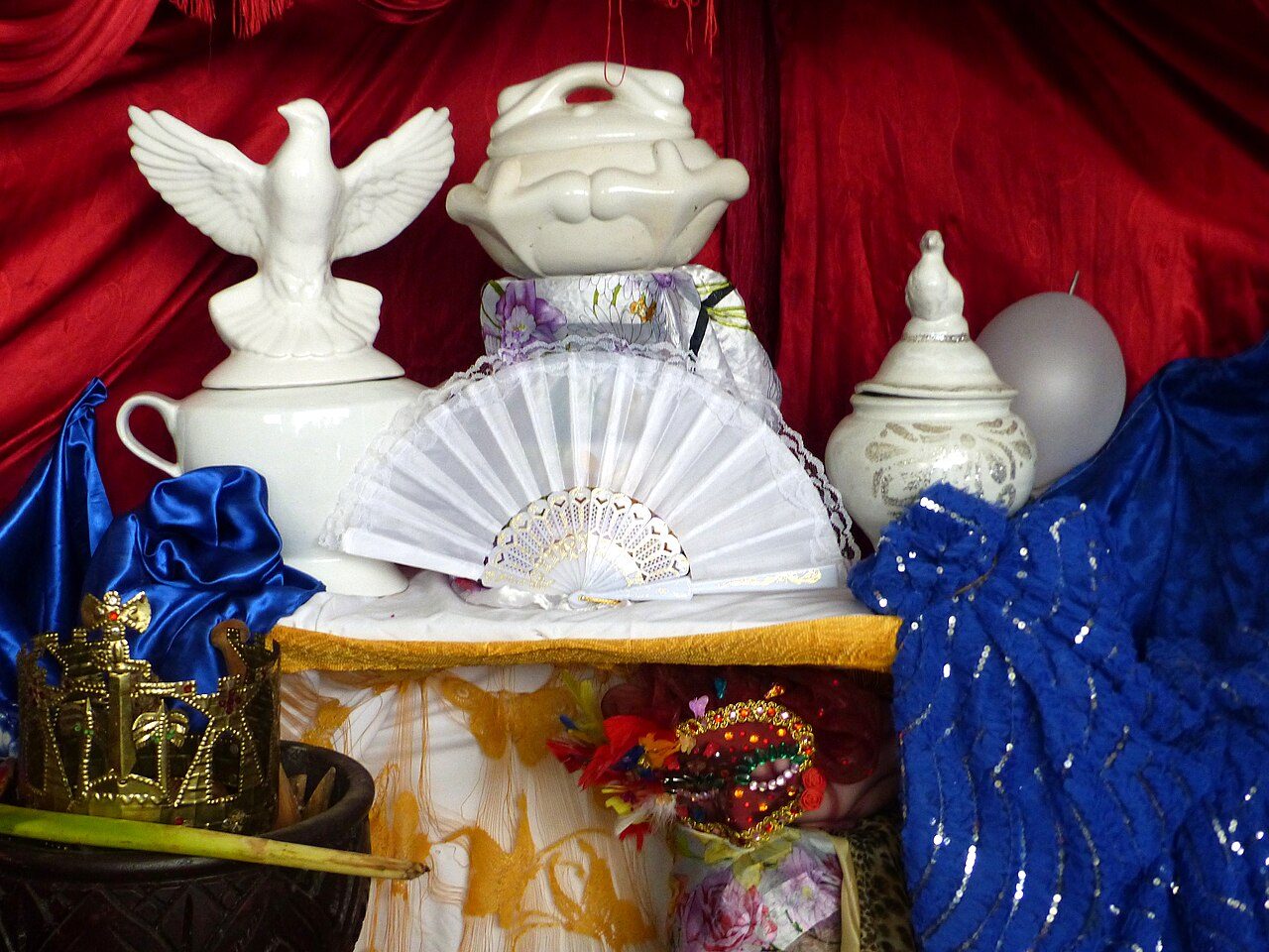 Altar de santería con soperas blancas, abanico, paloma y corona dorada sobre telas azules